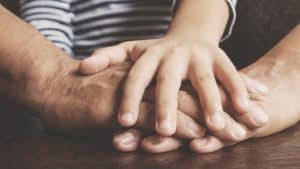 close up of child and parents hands laid on top of each other in team-like fashion