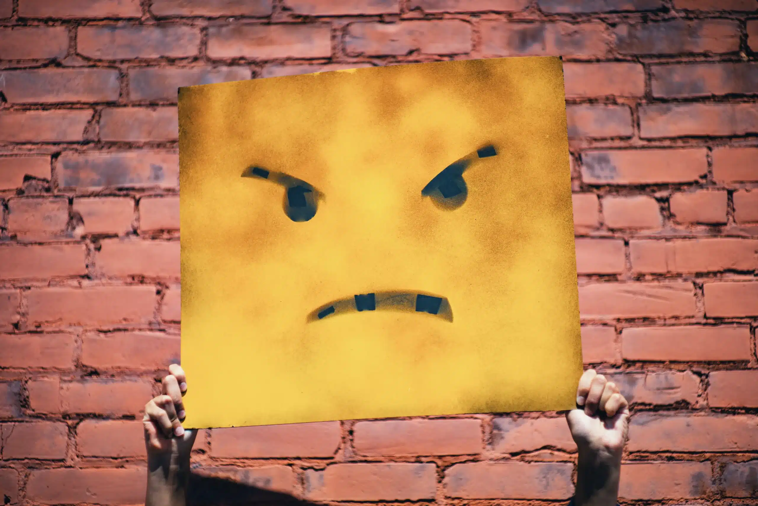 A square angry face against a brick wall