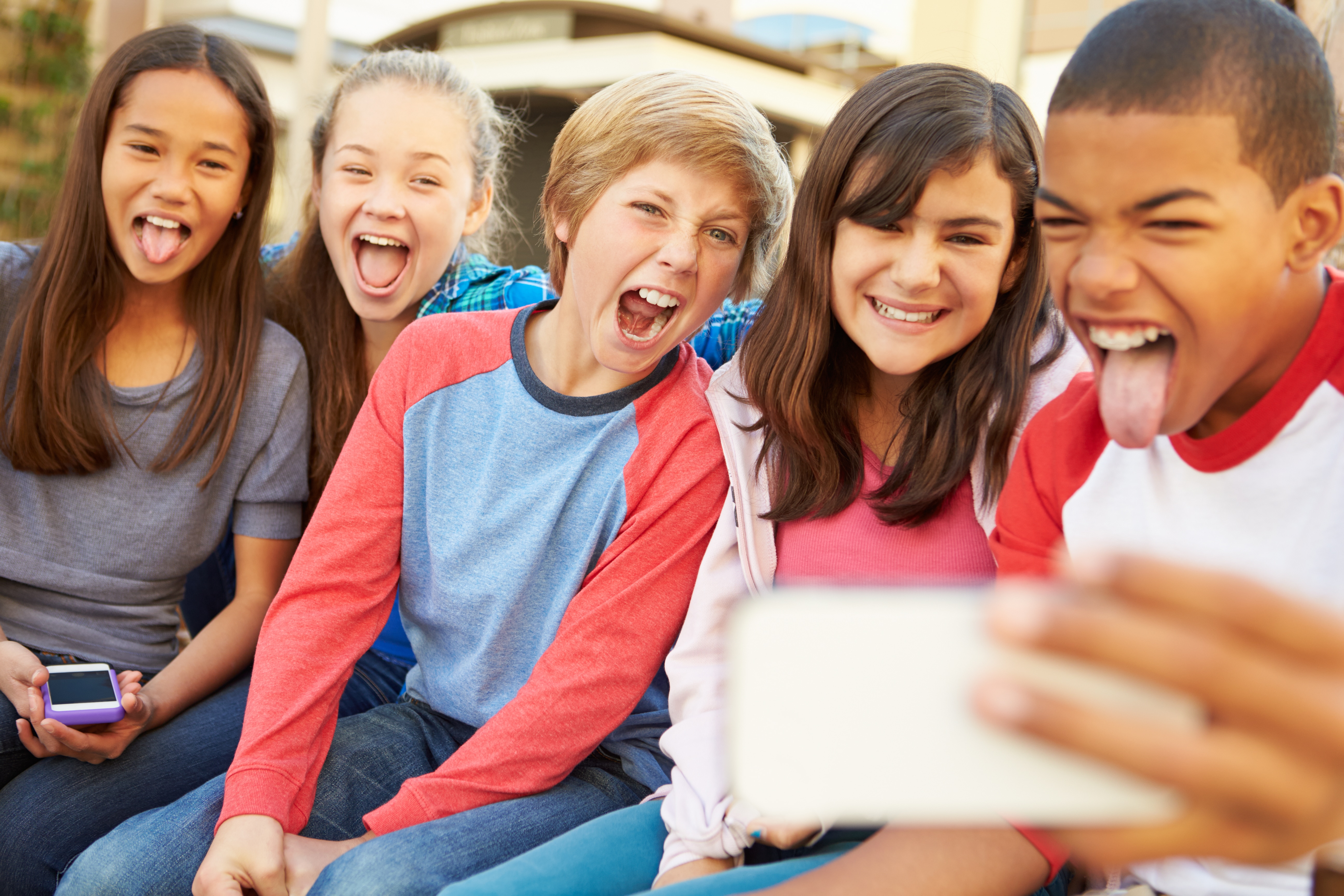 Group Of Children Sitting On Bench In Mall Taking Selfie Laughing And Smiling