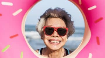 Older person wearing sunglasses smiling at a beach inside a donut image filter